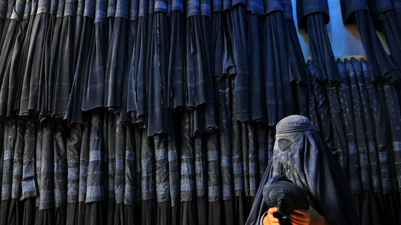 Une femme devant un magasin de burqa en Afghanistan. [SAYED MUSTAFA - Keystone]