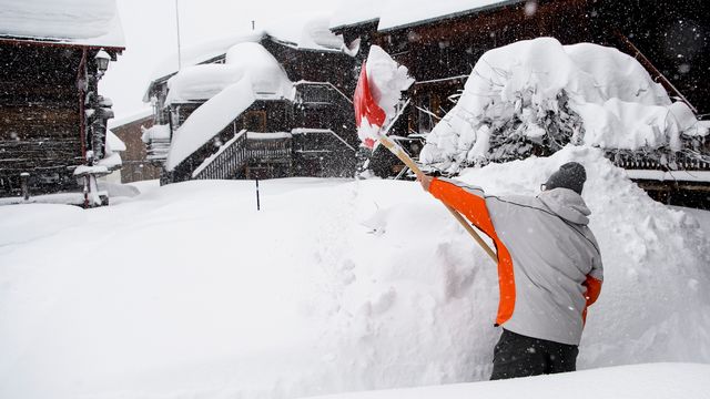 Une personne déblaie de la neige dimanche à Bellwald dans la Vallée de Conches en Valais. [Jean-Christophe Bott - Keystone]