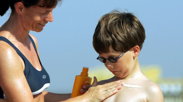 Une femme étale de la crème solaire sur le torse de son fils. (image d'illustration) [Joerg Sarbach - AP/Keystone]
