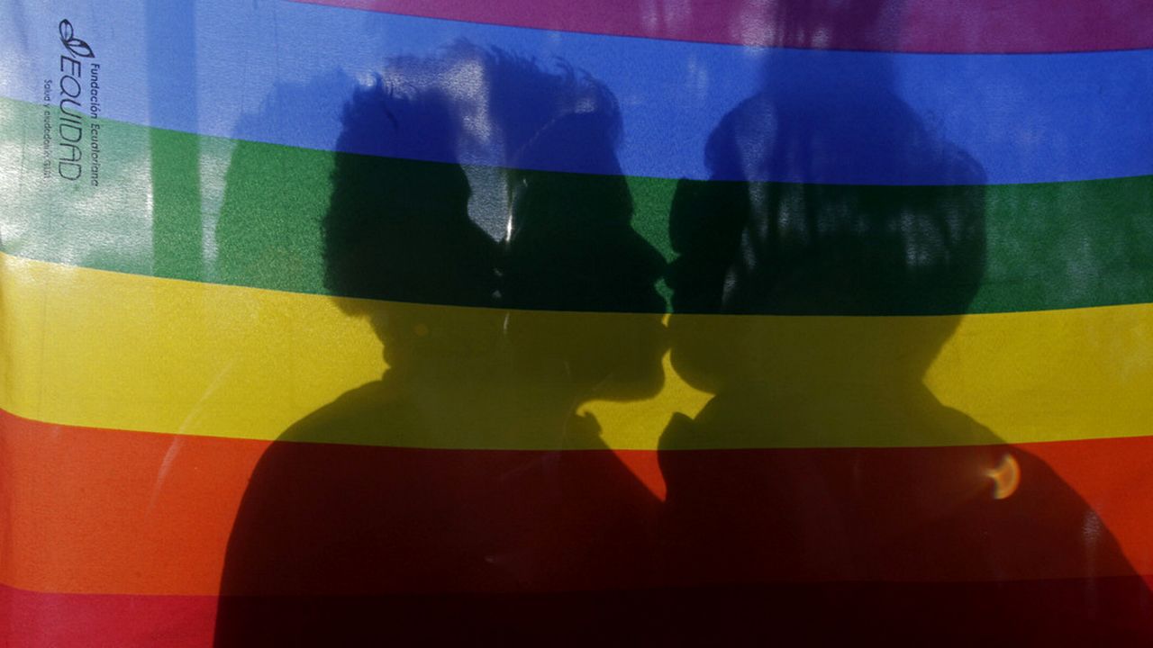 Un couple d'homosexuels s'embrase derrière un drapeau aux couleurs arc en ciel. [Dolores Ochoa - AP/Keystone]