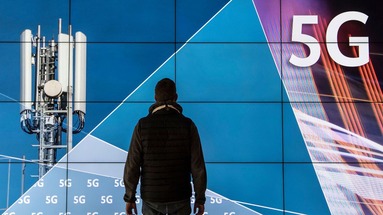 Un homme se tient devant un écran affichant une antenne 5G. [Boris Roessler - Keystone]