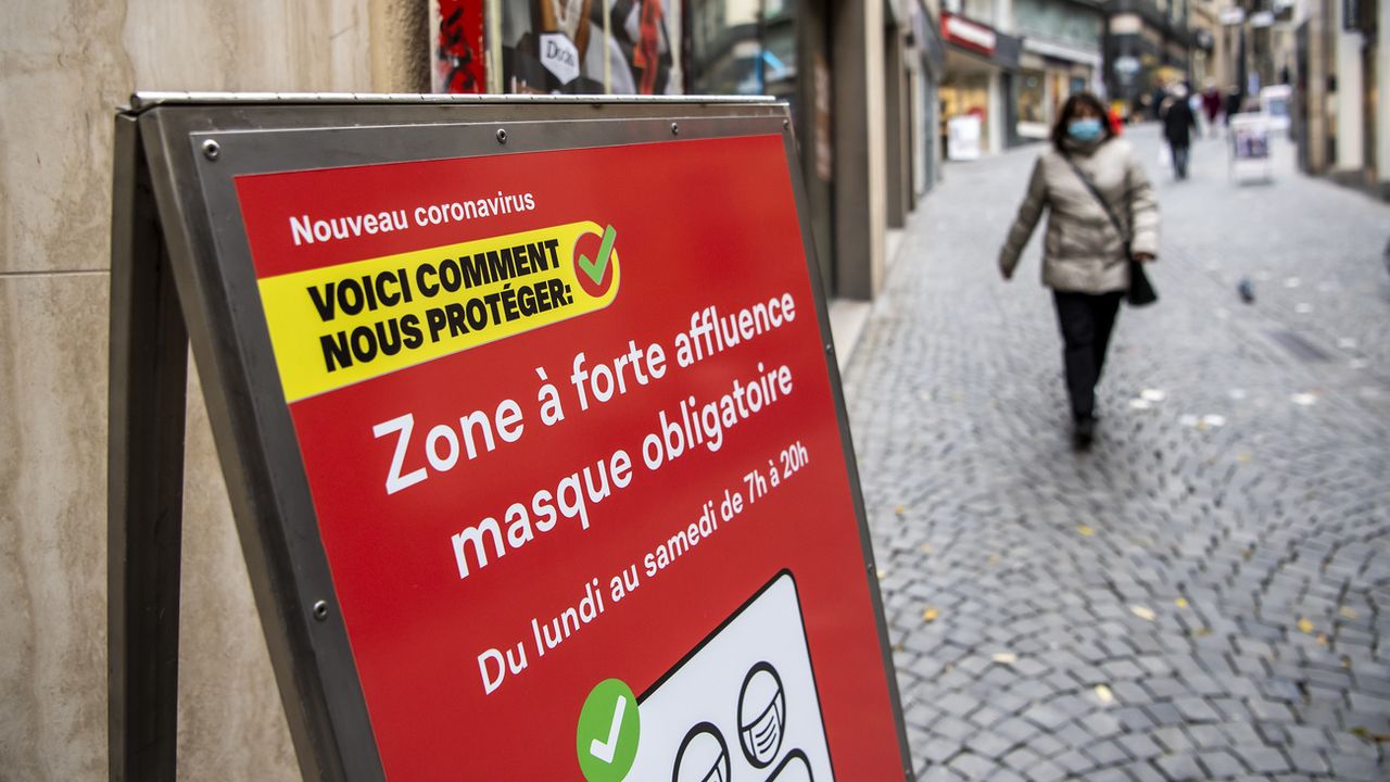 Une personne masquée près d'un panneau signalant une "zone à forte affluence", au centre-ville de Lausanne, le 10 novembre 2020. [Jean-Christophe Bott - Keystone]