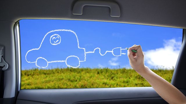 Un enfant dessine une voiture électrique sur la fenêtre d'une voiture. [tomwang - Depositphotos]