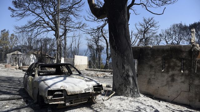 Une voiture et des maisons calcinées après un incendie dans le village de Lampiri en Grèce. [Andreas Alexopoulos - AP Photo]