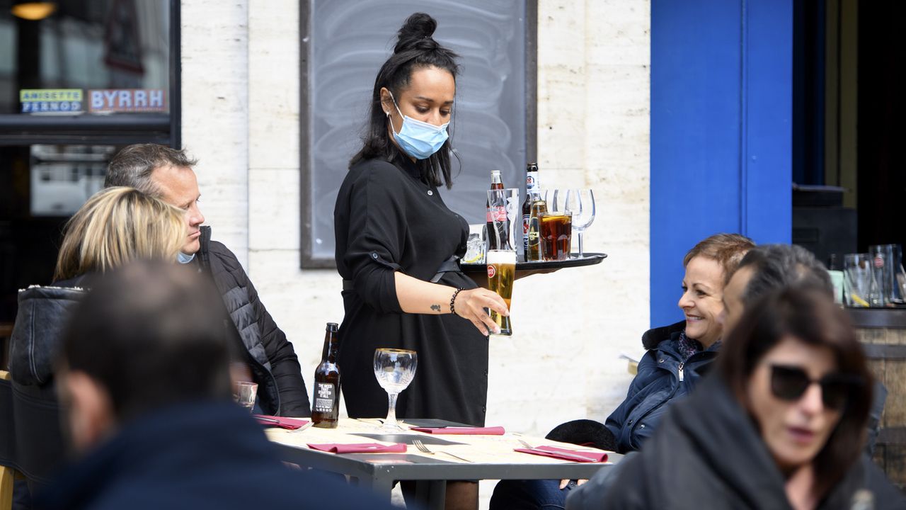 Une serveuse amène des boissons à une table en portant un masque. [Laurent Gillieron - KEYSTONE]