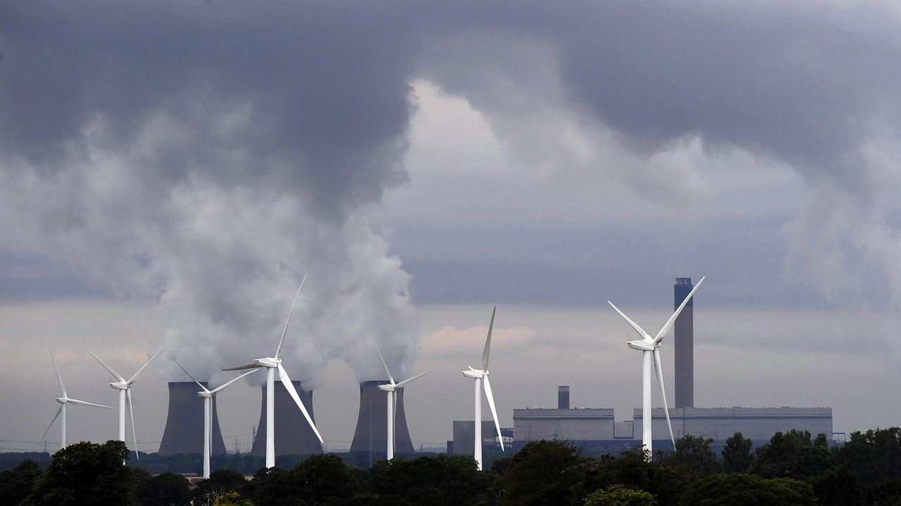 Une centrale à charbon côtoie une rangée d'éoliennes, à Drax en Angleterre. [John Giles - AP/Keystone]