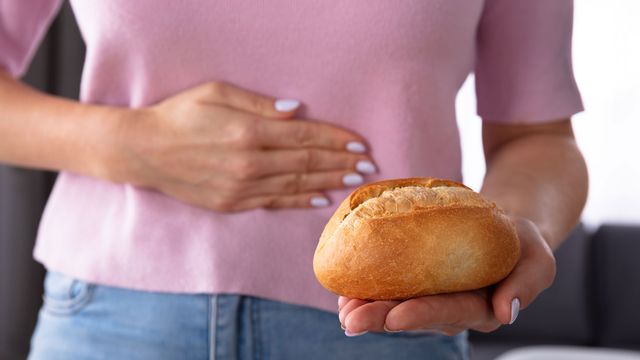 Une femme se tient de ventre en regardant un pain qu'elle tient dans sa main. [AndreyPopov - Depositphotos]
