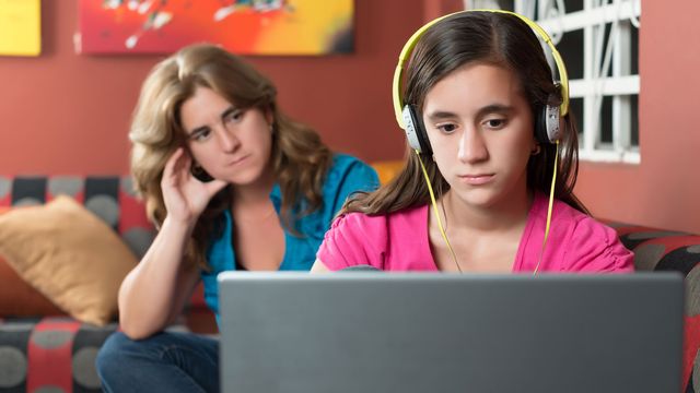 Une mère regarde sa fille jouer sur son ordinateur d'un air désapprobateur. [kmiragaya - Depositphotos]