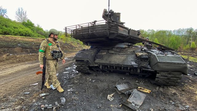 Un soldat ukrainien devant un char russe détruit dans la région de Kharkiv. [Vitalii Hnidyi - Reuters]