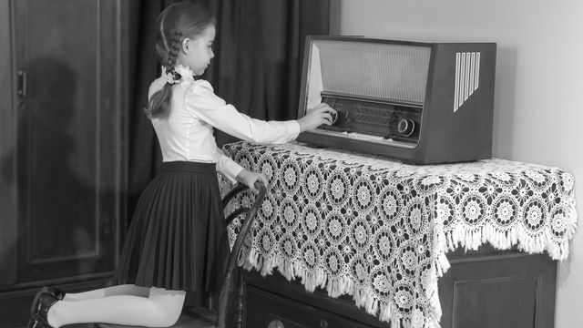 Une petite fille règle le volume d'une vieille radio. [lotosfoto1 - Depositphotos]