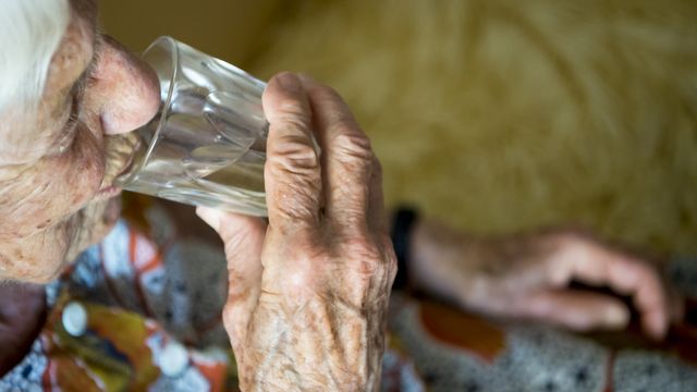 Une personne agée boit de l'eau.La canicule de 2018 a entraîné une mortalité accrue. [Jean-Christophe Bott - Keystone]