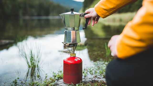 Un réchaud de camping et une cafetière au bord d'un lac. [Claudiumaxim - Depositphotos]
