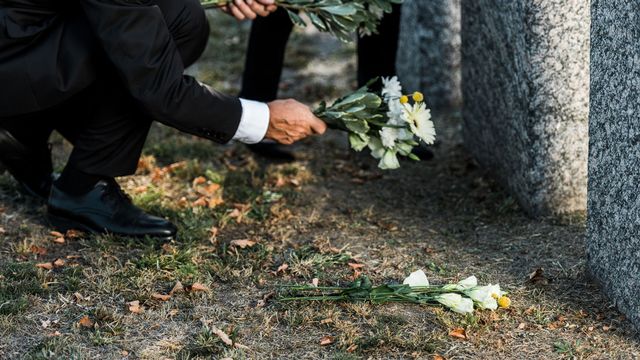 Gros plan sur les mains d'une personne qui pose des fleurs sur une tombe. [AndrewLozovyi - Depositphotos]