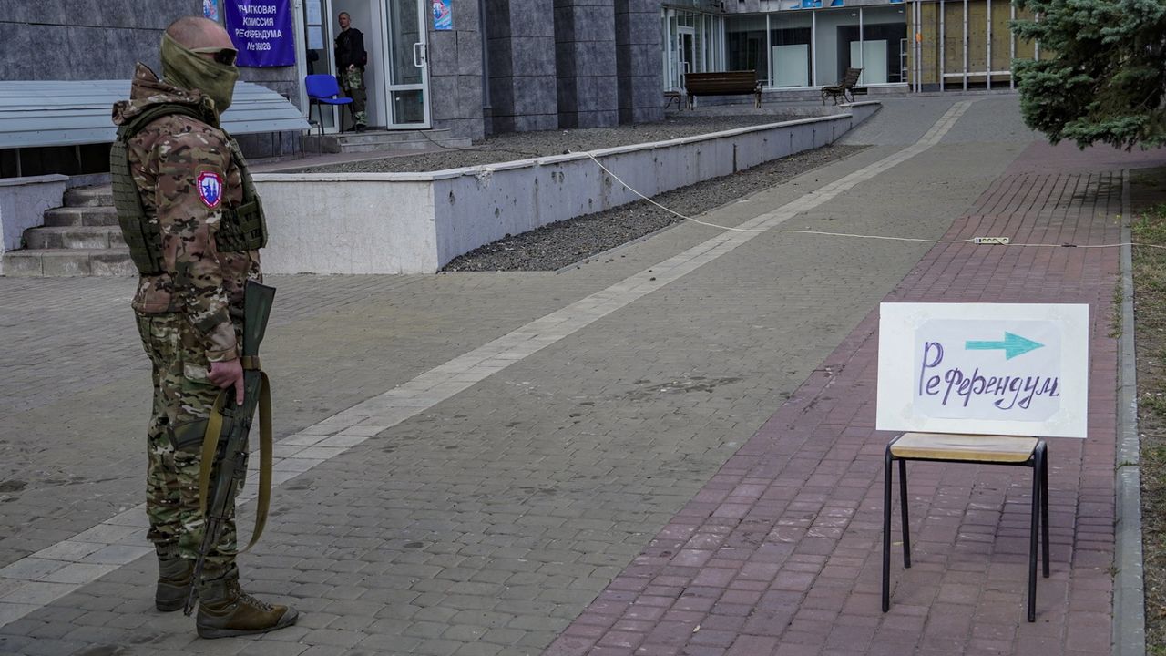 Un militaire russe monte la garde près d'un panneau indiquant "Référendum" à Marioupol le 25 septembre 2022. [Stringer - Keystone/EPA]