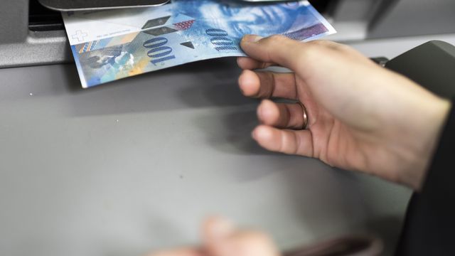 Une personne retire de l'argent dans un bancomat à Zurich. [Christian Beutler - Keystone]