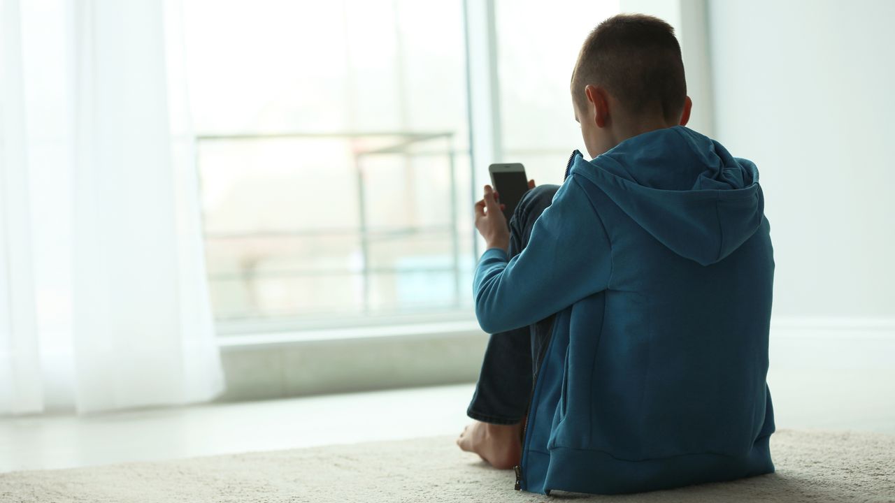 Un enfant bouleversé regarde son smartphone. [NewAfrica - Depositphotos]