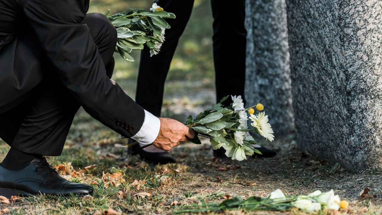 Un homme âgé dépose des fleurs près d'une pierre tombale. [Andrew Lozovyi - Depositphotos]