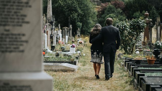 Deux personnes vues de dos marchent dans un cimetière. [Rawpixel - Depositphotos]