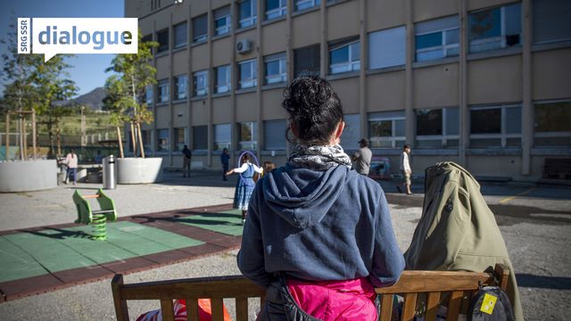Deux personnes migrantes sur un banc sur un eplace de jeux située à l'extérieur du centre fédéral d'asile à Balerna, au Tessin. [Francesca Agosta - Keystone/Ti-Press]